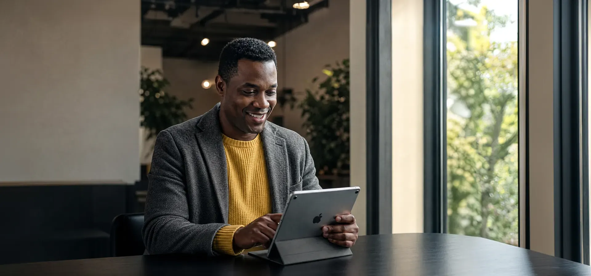 Profissional brasileiro sorrindo enquanto usa um tablet junto a uma janela